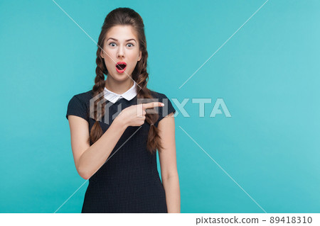 Amazement, wondered woman pointing finger right, at copy space. Studio shot, blue background Amazement, wondered woman pointing finger right, at copy space. Studio shot, blue background 89418310