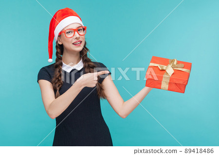 Business woman pointing finger on gift box and looking at camera and toothy smile. On green background. Studio shot 89418486