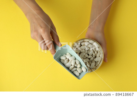 Female hands hold jar and scoop with white beans on yellow background Female hands hold jar and scoop with white beans on yellow background 89418667