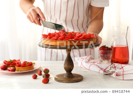 Woman in apron cut the strawberry tart Woman in apron cut the strawberry tart 89418744