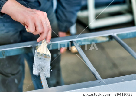 Working painter paints metal ladder with paint brush. Hand close-up with space for copying Working painter paints metal ladder with paint brush. Hand close-up with space for copying 89419735
