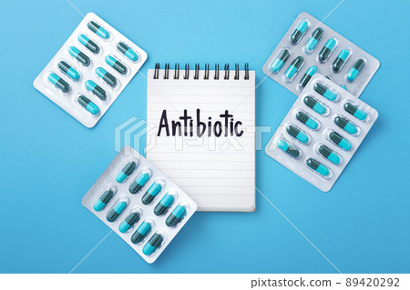 Antibiotic word on notebook with capsule pills in pack on blue background, top view 89420292