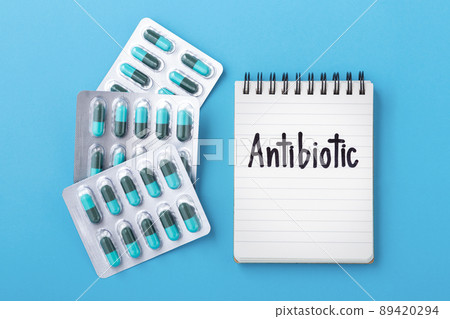 Antibiotic capsule pills in pack with notebook on blue background, top view 89420294