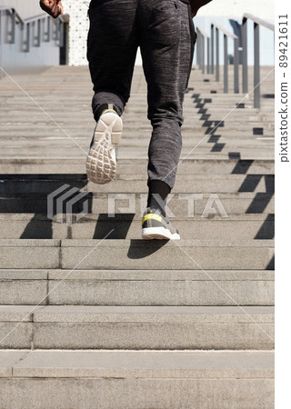Effective step running workout. Rear view of legs of unrecognizable male athlete running up concrete stairs outdoors 89421611