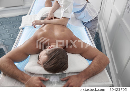 Man lies on couch while woman therapist does back massage with elbow in hospital office 89423705