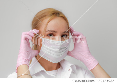 The doctor puts on a mask. Close-up portrait of medical staff. A woman in a protective mask .Isolated on a white background. Healthcare, cosmetology and medical concept The doctor puts on a mask. Close-up portrait of medical staff. A woman in a protective mask .Isolated on a white background. Healthcare, cosmetology and medical concept 89423982