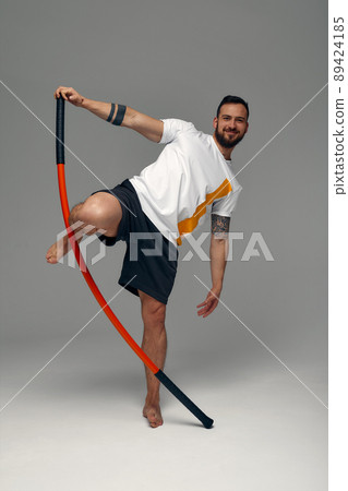 A fighter in white t-shirt and black shorts, stands in a fighting artificially pose and holds a fight stick on studio background. A fighter in white t-shirt and black shorts, stands in a fighting artificially pose and holds a fight stick on studio background. 89424185