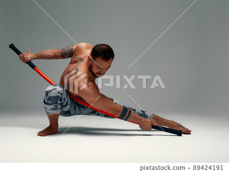 A ninja man holds on to a fighting stick and attacks close-up on gray studio background A ninja man holds on to a fighting stick and attacks close-up on gray studio background 89424191