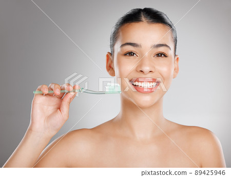 Call it insurance for your teeth. Studio shot of an attractive young woman brushing her teeth against a grey background. 89425946
