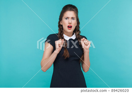 Shocked young woman looking at camera with stress. Indoor, studio shot on blue background Shocked young woman looking at camera with stress. Indoor, studio shot on blue background 89426020