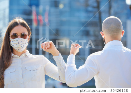 Instead of greeting with hug or handshake man and woman bump elbows on a street. 89426128