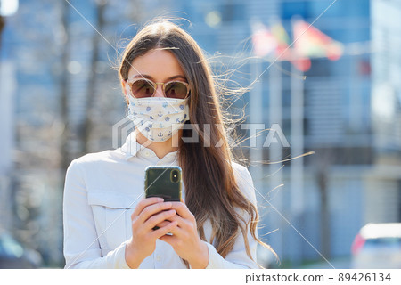 A woman wears a face mask to avoid the spread of coronavirus using a smartphone. A woman wears a face mask to avoid the spread of coronavirus using a smartphone. 89426134