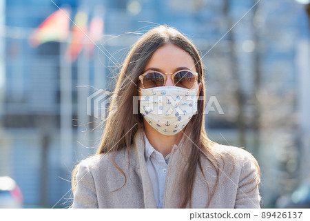 A woman in a coat wears a medical face mask to avoid the spread of coronavirus. 89426137