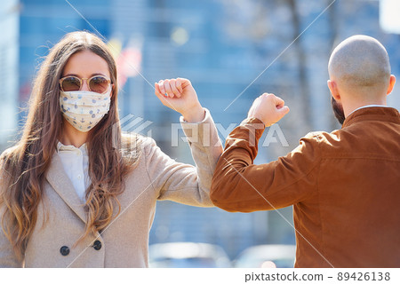 Instead of greeting with hug or handshake man and woman bump elbows on a street. 89426138