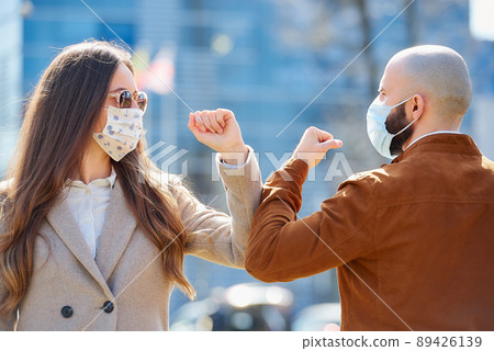 Instead of greeting with hug or handshake man and woman bump elbows on a street. 89426139