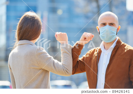 Instead of greeting with hug or handshake man and woman bump elbows on a street. Instead of greeting with hug or handshake man and woman bump elbows on a street. 89426141