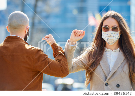 Instead of greeting with hug or handshake man and woman bump elbows on a street. Instead of greeting with hug or handshake man and woman bump elbows on a street. 89426142