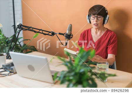 Portrait of mature woman wearing headphones and talking at online radio station - podcast and broadcast concept 89426296