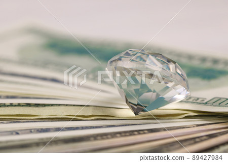 US money bills with large diamond close up. Big amount of dollars and huge transparent gem on table. Business and jewellery US money bills with large diamond close up. Big amount of dollars and huge transparent gem on table. Business and jewellery 89427984