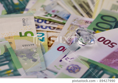 Euro and dollar money bills and coins with large diamond close up. Big amount of money and huge transparent gem on table. Business and jewellery 89427990
