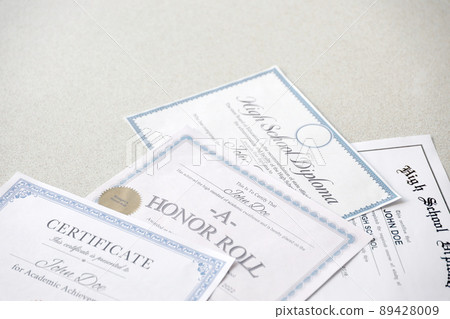 A honor roll recognition, certificate of achievement and high school diploma lies on table. Education documents 89428009