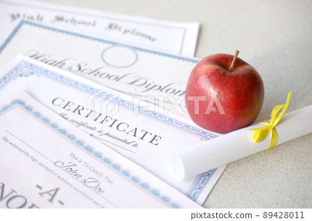 A honor roll recognition, certificate of achievement and high school diploma lies on table with small scroll and red apple. Education documents A honor roll recognition, certificate of achievement and high school diploma lies on table with small scroll and red apple. Education documents 89428011