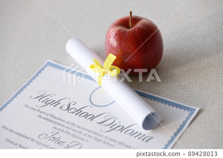 A high school diploma lies on table with small scroll and red apple. Education documents A high school diploma lies on table with small scroll and red apple. Education documents 89428013