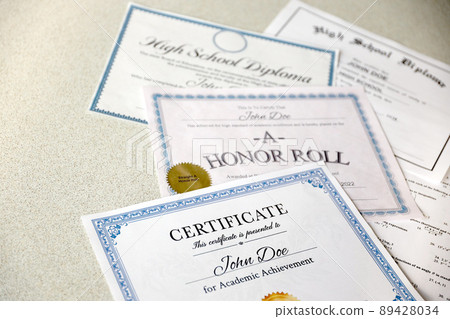 A honor roll recognition, certificate of achievement and high school diploma lies on table. Education documents 89428034