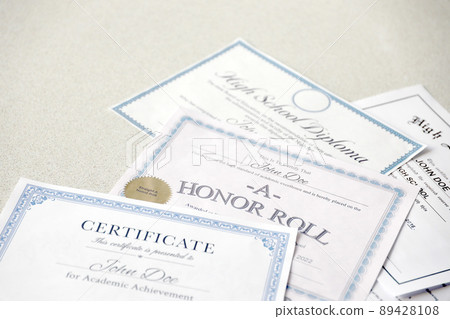 A honor roll recognition, certificate of achievement and high school diploma lies on table. Education documents A honor roll recognition, certificate of achievement and high school diploma lies on table. Education documents 89428108