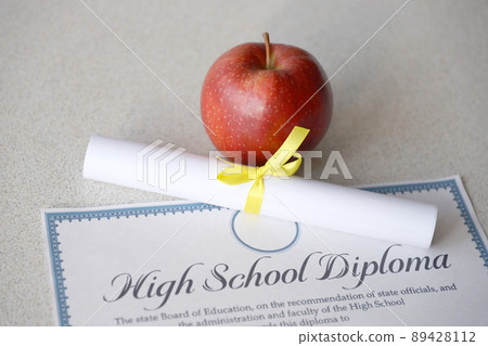 A high school diploma lies on table with small scroll and red apple. Education documents A high school diploma lies on table with small scroll and red apple. Education documents 89428112