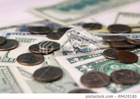 US money bills and coins with large diamond close up. Big amount of dollars and huge transparent gem on table. Business and jewellery 89428180