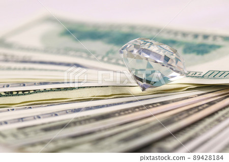 US money bills with large diamond close up. Big amount of dollars and huge transparent gem on table. Business and jewellery US money bills with large diamond close up. Big amount of dollars and huge transparent gem on table. Business and jewellery 89428184