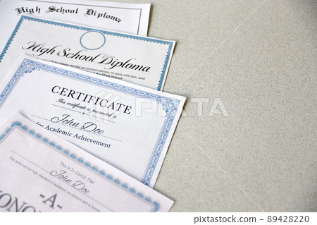 A honor roll recognition, certificate of achievement and high school diploma lies on table. Education documents A honor roll recognition, certificate of achievement and high school diploma lies on table. Education documents 89428220
