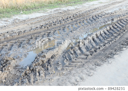 Autumn landscape with a curved road and traces of the tread of large wheels of agricultural machinery Autumn landscape with a curved road and traces of the tread of large wheels of agricultural machinery 89428231