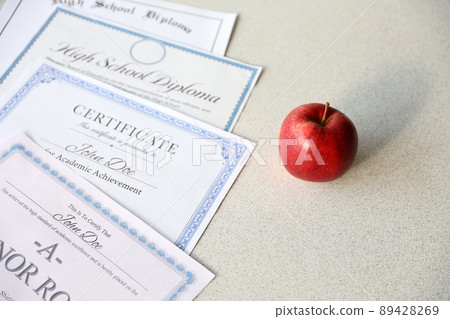 A honor roll recognition, certificate of achievement and high school diploma lies on table with red apple. Education documents A honor roll recognition, certificate of achievement and high school diploma lies on table with red apple. Education documents 89428269