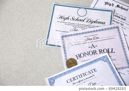 A honor roll recognition, certificate of achievement and high school diploma lies on table. Education documents A honor roll recognition, certificate of achievement and high school diploma lies on table. Education documents 89428283