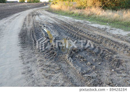 Autumn landscape with a curved road and traces of the tread of large wheels of agricultural machinery Autumn landscape with a curved road and traces of the tread of large wheels of agricultural machinery 89428284