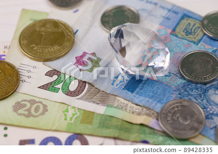 Ukrainian money bills and diamond close up. Big amount of hryvnia bills and large perfect gem on table. Business and jewellery Ukrainian money bills and diamond close up. Big amount of hryvnia bills and large perfect gem on table. Business and jewellery 89428335