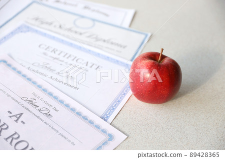 A honor roll recognition, certificate of achievement and high school diploma lies on table with red apple. Education documents A honor roll recognition, certificate of achievement and high school diploma lies on table with red apple. Education documents 89428365
