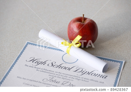 A high school diploma lies on table with small scroll and red apple. Education documents A high school diploma lies on table with small scroll and red apple. Education documents 89428367