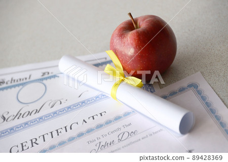 A honor roll recognition, certificate of achievement and high school diploma lies on table with small scroll and red apple. Education documents A honor roll recognition, certificate of achievement and high school diploma lies on table with small scroll and red apple. Education documents 89428369