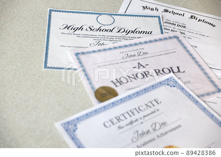 A honor roll recognition, certificate of achievement and high school diploma lies on table. Education documents A honor roll recognition, certificate of achievement and high school diploma lies on table. Education documents 89428386