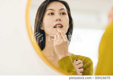 Woman applying lipstick in front of the mirror 89428670