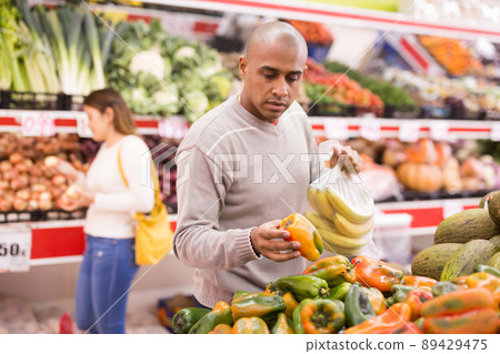 Buyer selects ripe bell peppers in the vegetable section of supermarket 89429475