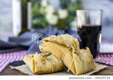 Traditional Andean corn and meat tamales served on a wooden board on a still life table with a glass of wine. Regional food. copy space. Traditional Andean corn and meat tamales served on a wooden board on a still life table with a glass of wine. Regional food. copy space. 89429724