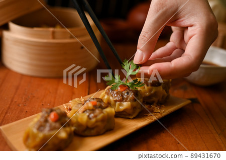 Female chef using chopsticks, garnishing steamed pork or meat dumplings with coriander leaf. Female chef using chopsticks, garnishing steamed pork or meat dumplings with coriander leaf. 89431670