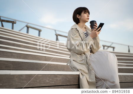 A woman sitting on the stairs with a smartphone and coffee in her hand 89431938