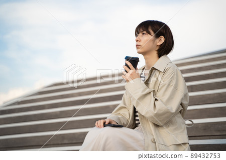 A woman sitting on the stairs with a smartphone and coffee in her hand 89432753
