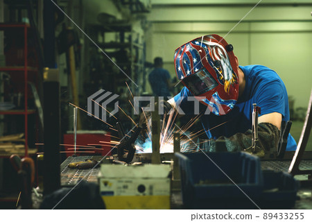 Professional Heavy Industry Welder Working Inside factory, Wears Helmet and Starts Welding. Selective Focus Professional Heavy Industry Welder Working Inside factory, Wears Helmet and Starts Welding. Selective Focus 89433255
