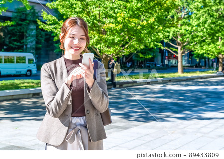 A young business woman operating a smartphone in Tokyo Marunouchi A young business woman operating a smartphone in Tokyo Marunouchi 89433809